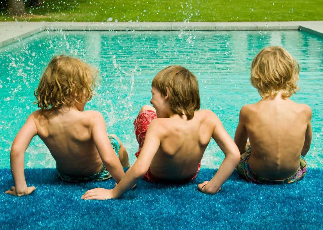 Children sitting on Condor Grass artificial grass at the edge of a pool